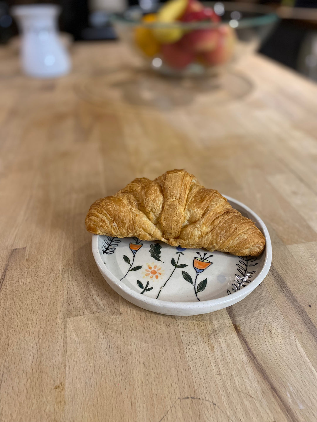 Croissant on a decorative plate with a fruit bowl in the background