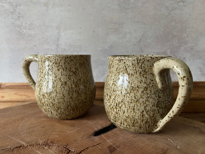 Two ceramic mugs with speckled glaze on a wooden surface with a gray background