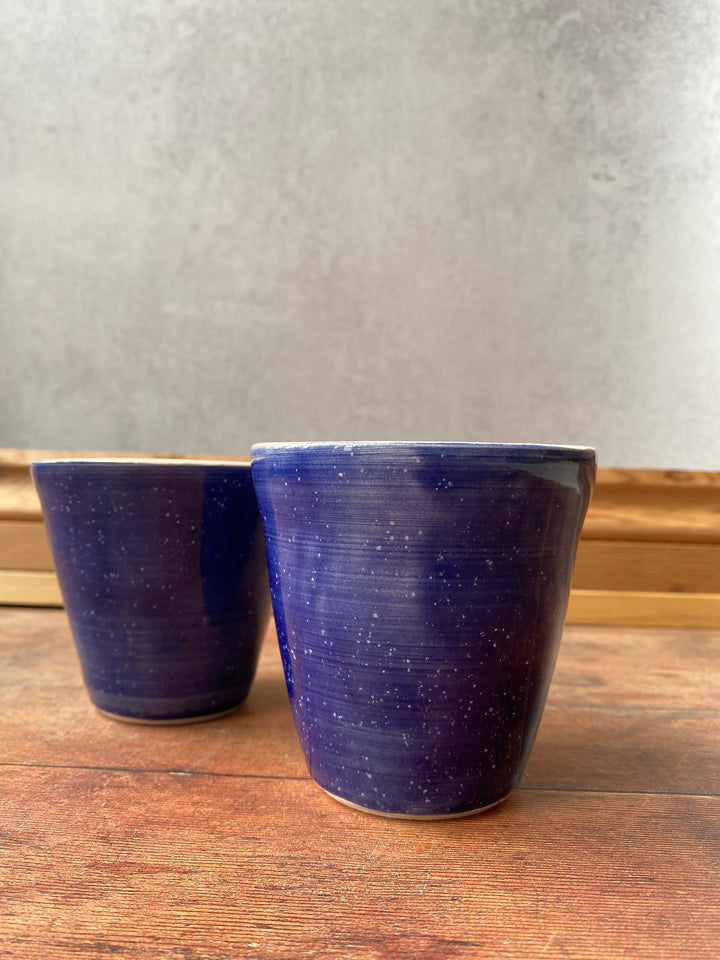 Handmade evening sky blue flared ceramic coffee cup sitting on a rustic wooden table UK