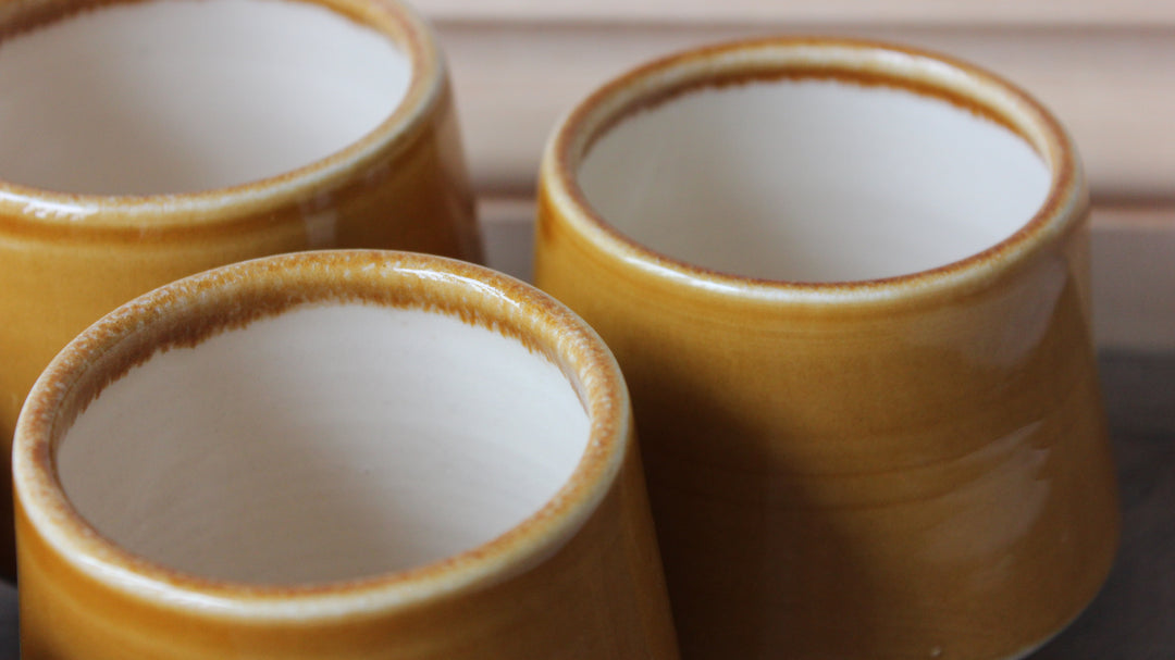 Three small ceramic cups with a glossy mustard-yellow glazed exterior and a white interior, shown in a close-up shot.
