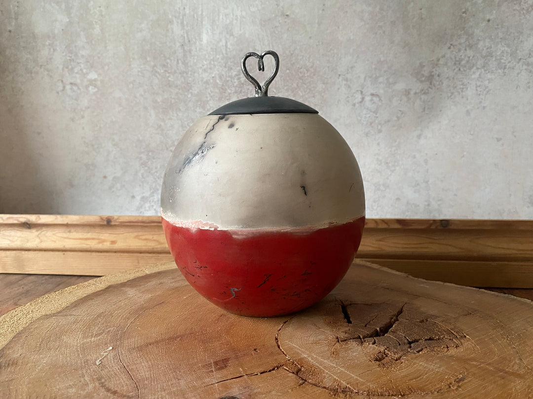 Spherical metal object with a heart-shaped handle on a wooden surface