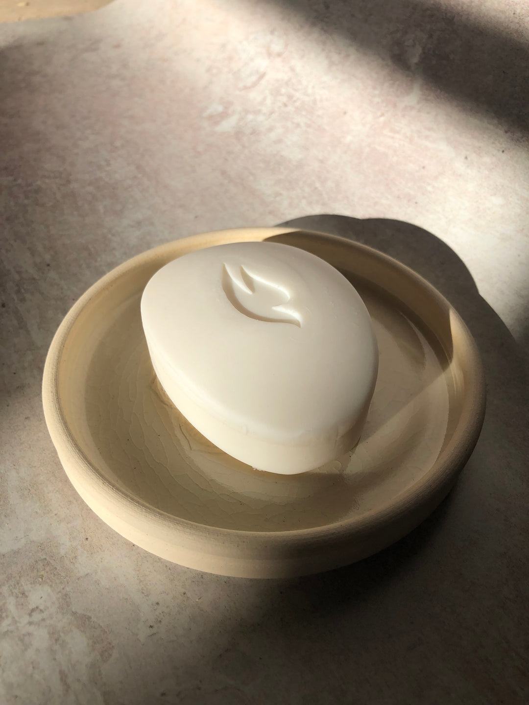Close-up of a white ceramic bowl with a bar of soap on a textured surface