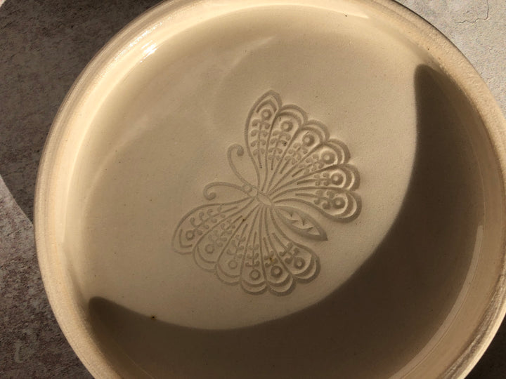 Beige ceramic dish with a butterfly design on a dark surface