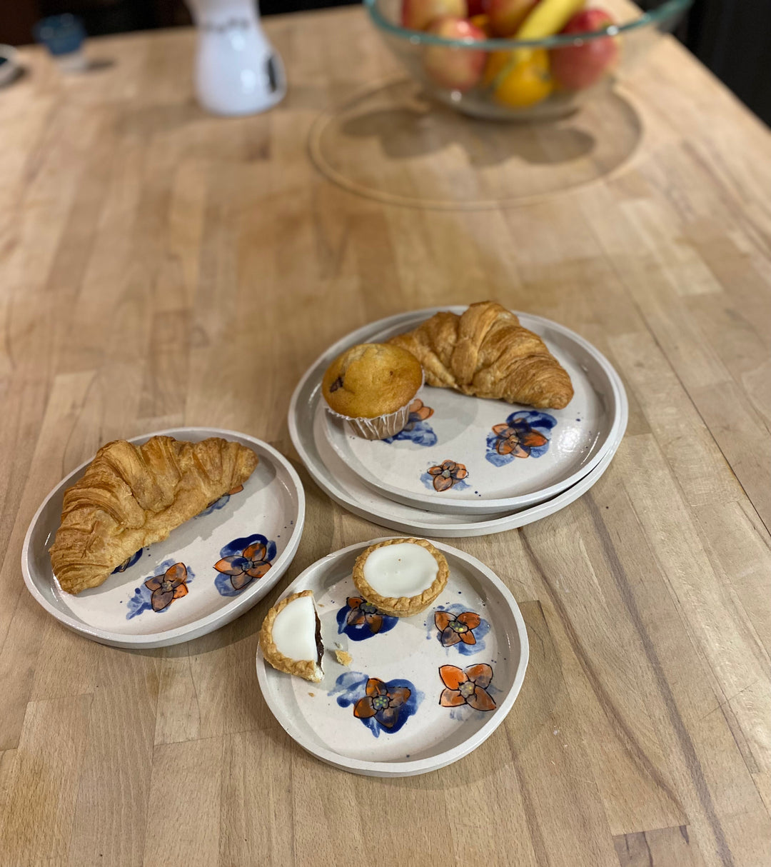 Three small ceramic plates with floral designs on a wooden table, each containing a pastry.