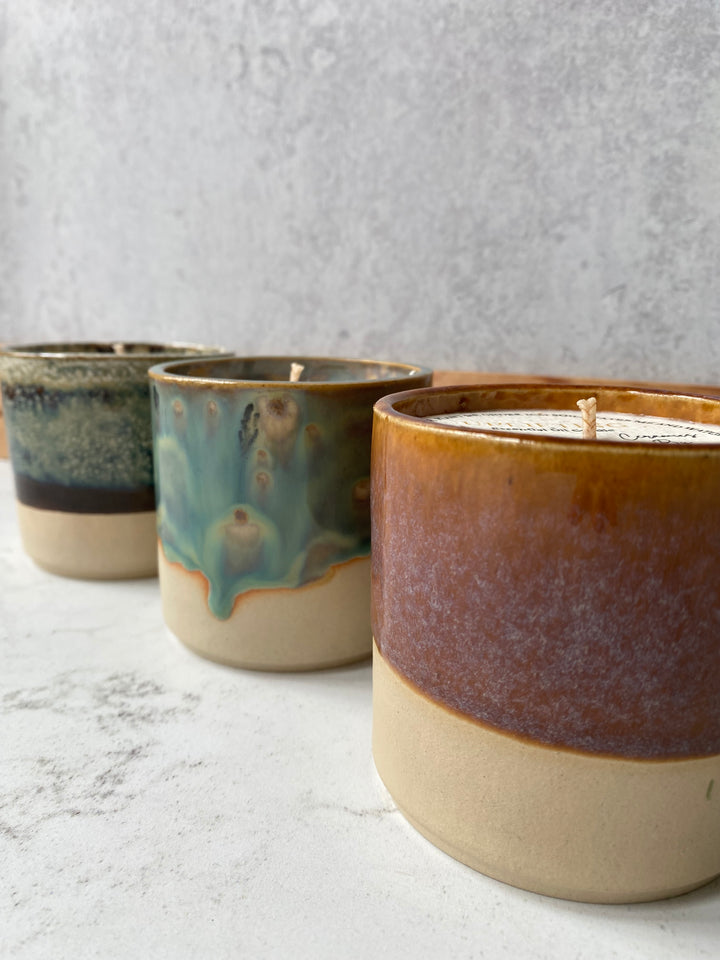 Four ceramic wall candles with varying glazes and colors, arranged diagonally against a textured light gray wall.