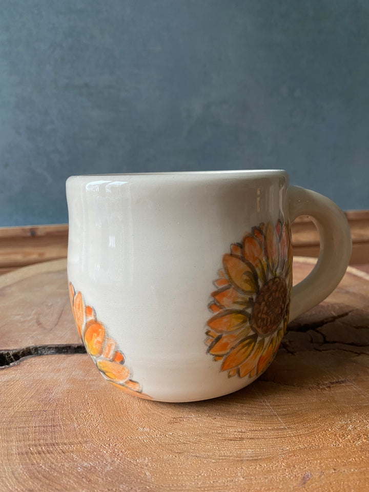 White mug with sunflower design on a wooden surface