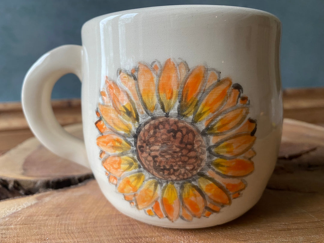 White mug with a sunflower design on a wooden surface