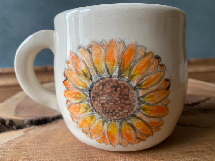 White mug with a sunflower design on a wooden surface