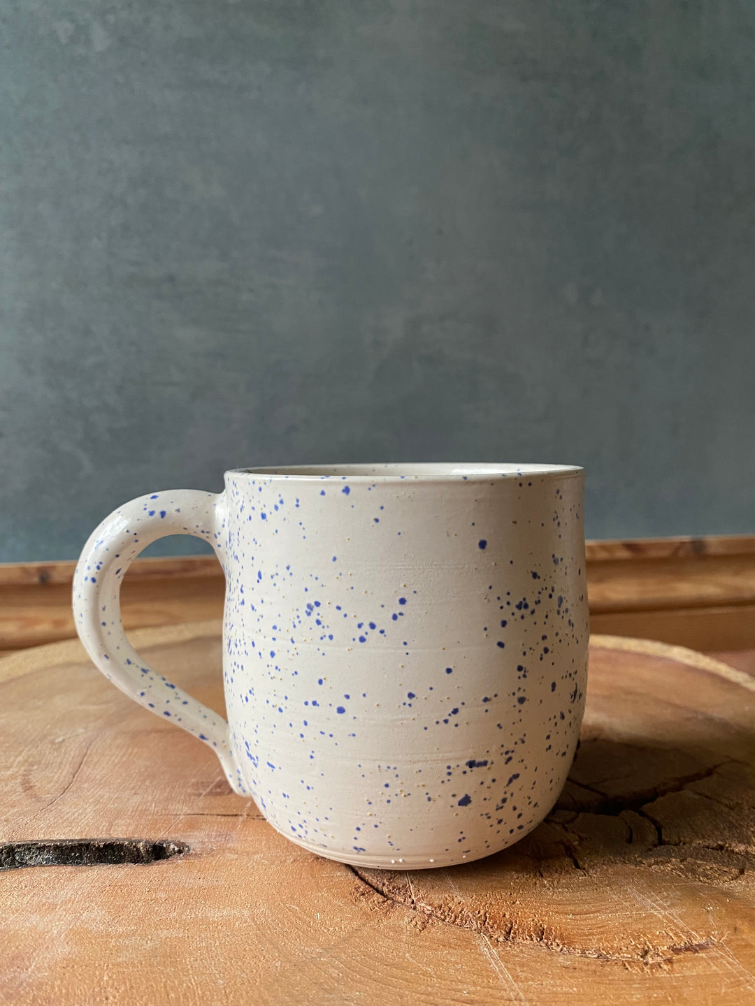 Speckled ceramic mug on a wooden surface with a grey background