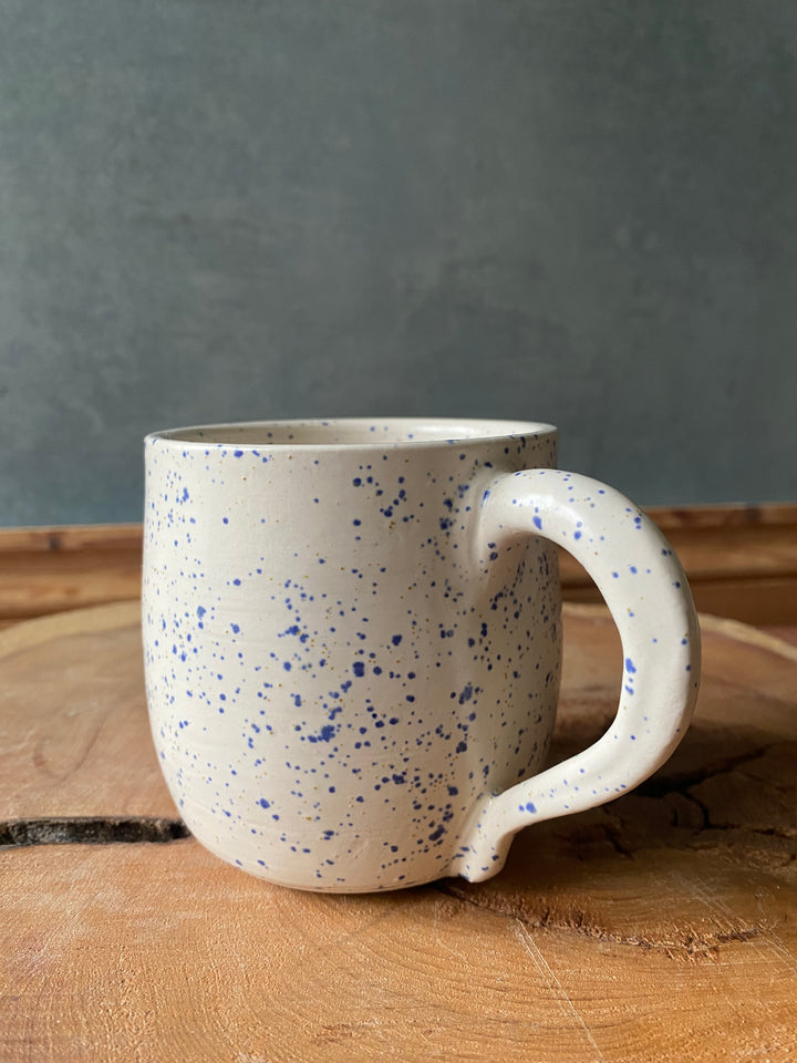 Speckled ceramic mug leaning against a wooden surface with a grey background