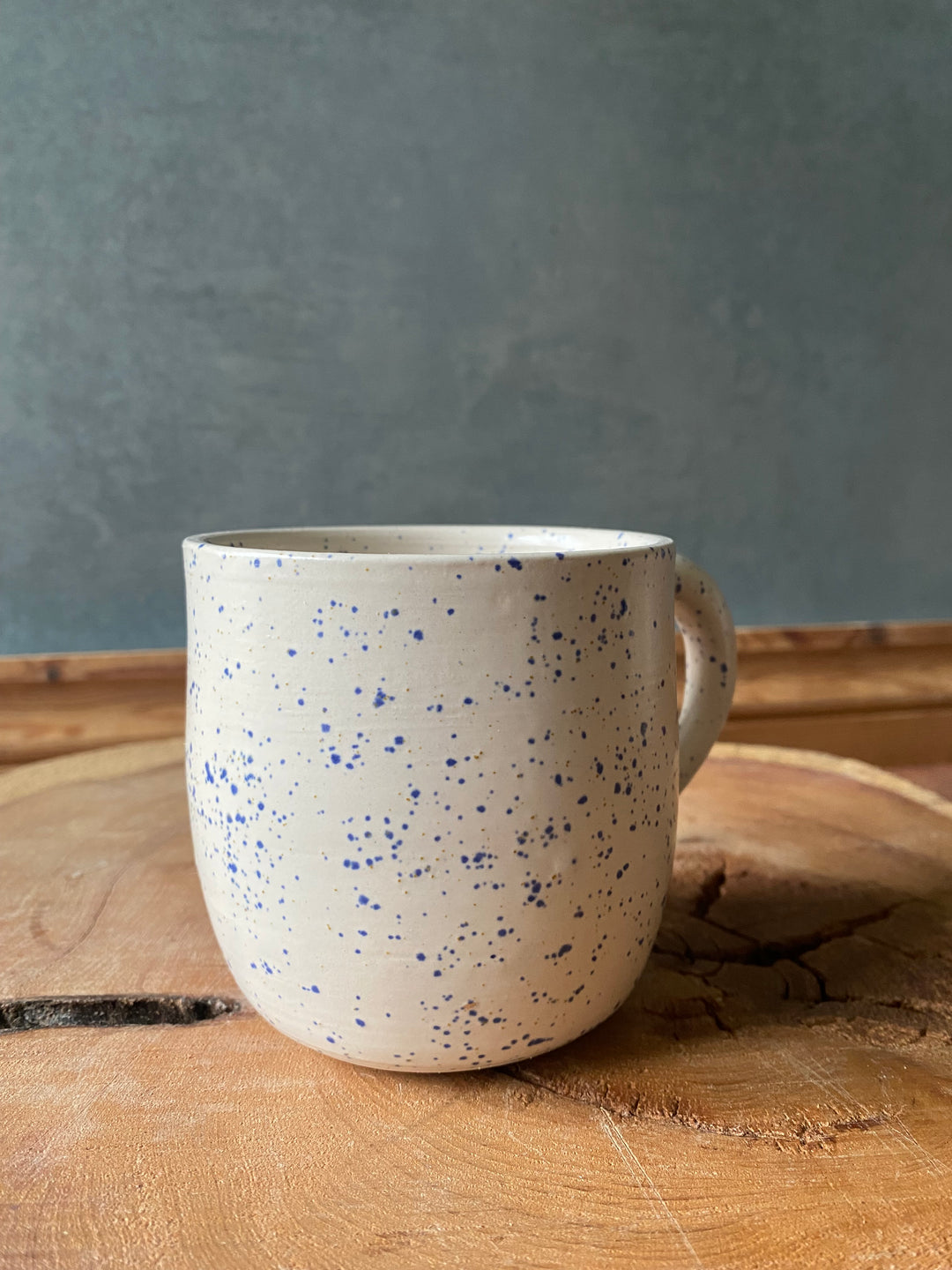 Speckled ceramic cup on a wooden surface with a grey background