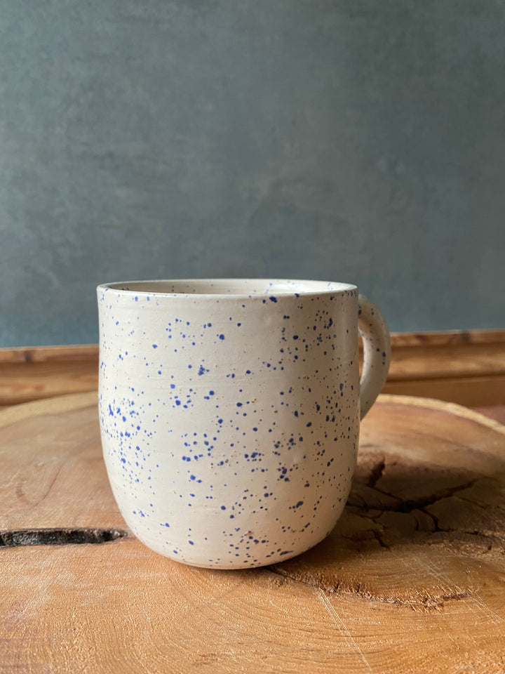 Speckled ceramic cup on a wooden surface with a grey background