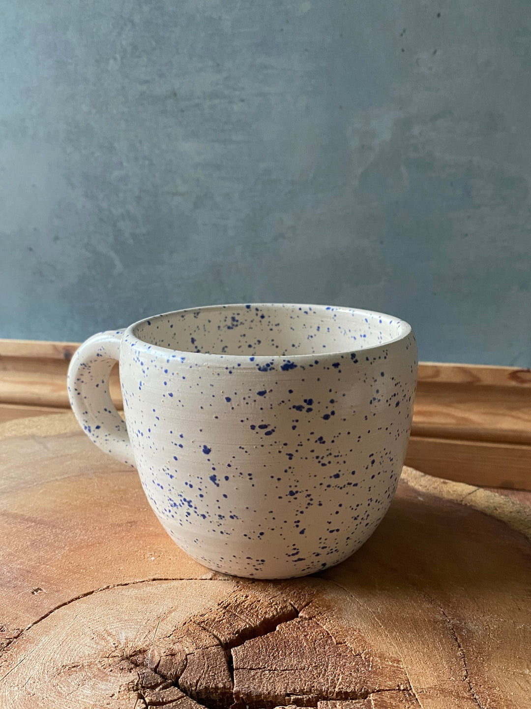 Speckled ceramic mug on a wooden surface with a grey background