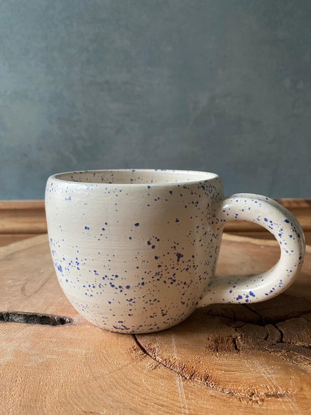 Speckled ceramic mug leaning against a wooden surface with a grey background