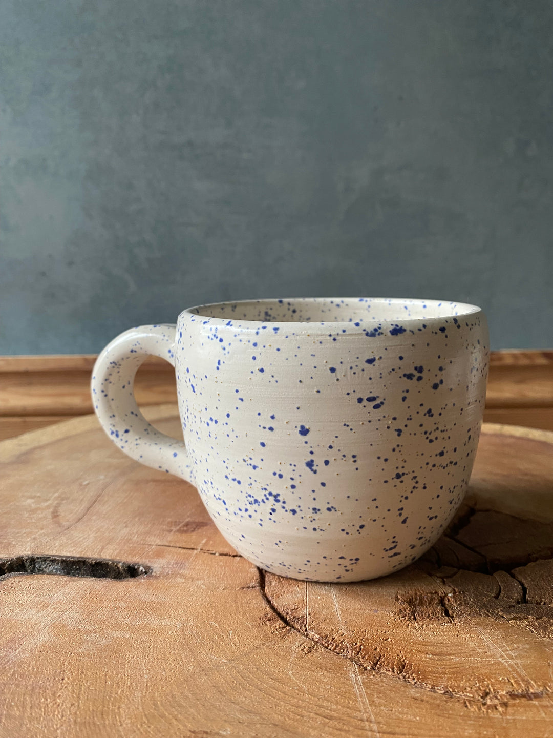 Speckled ceramic mug on a wooden surface with a grey background