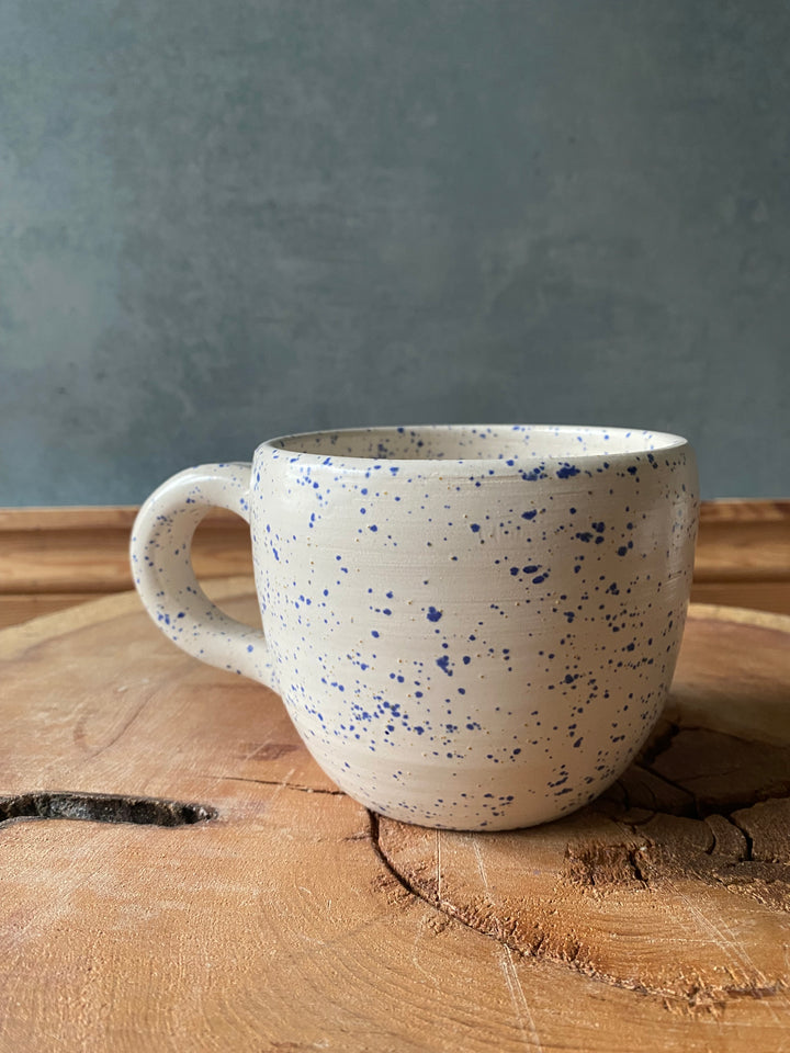 Speckled ceramic mug on a wooden surface with a grey background