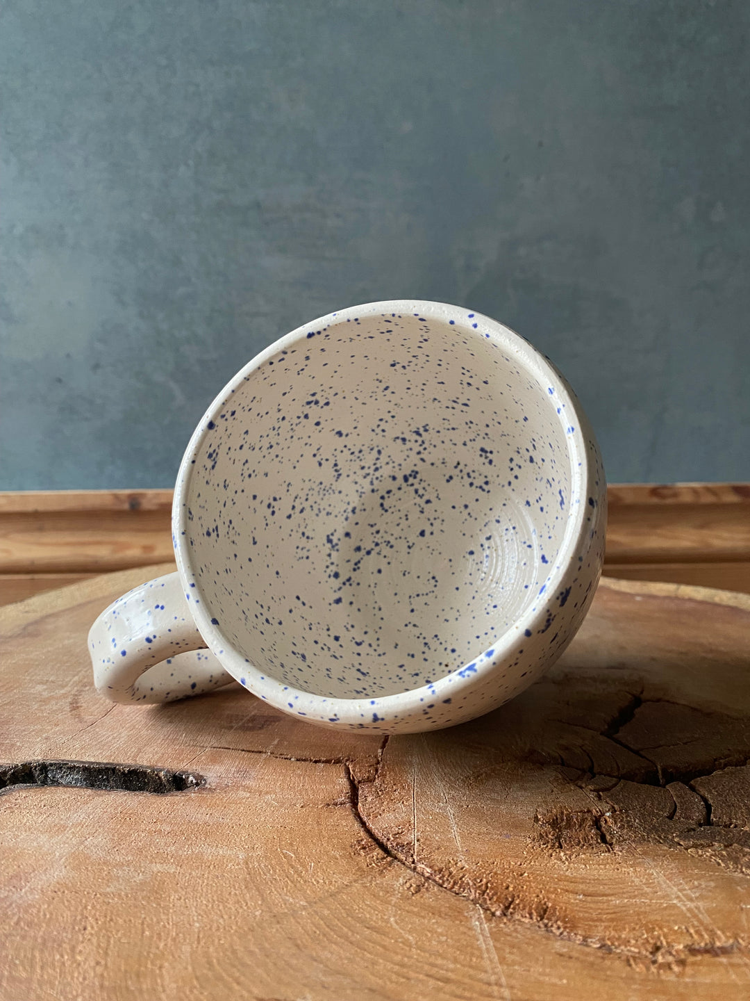 Speckled ceramic mug on a wooden surface with a grey background