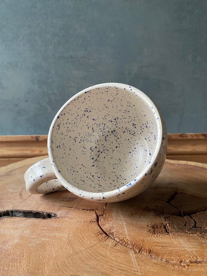 Speckled ceramic mug on a wooden surface with a grey background