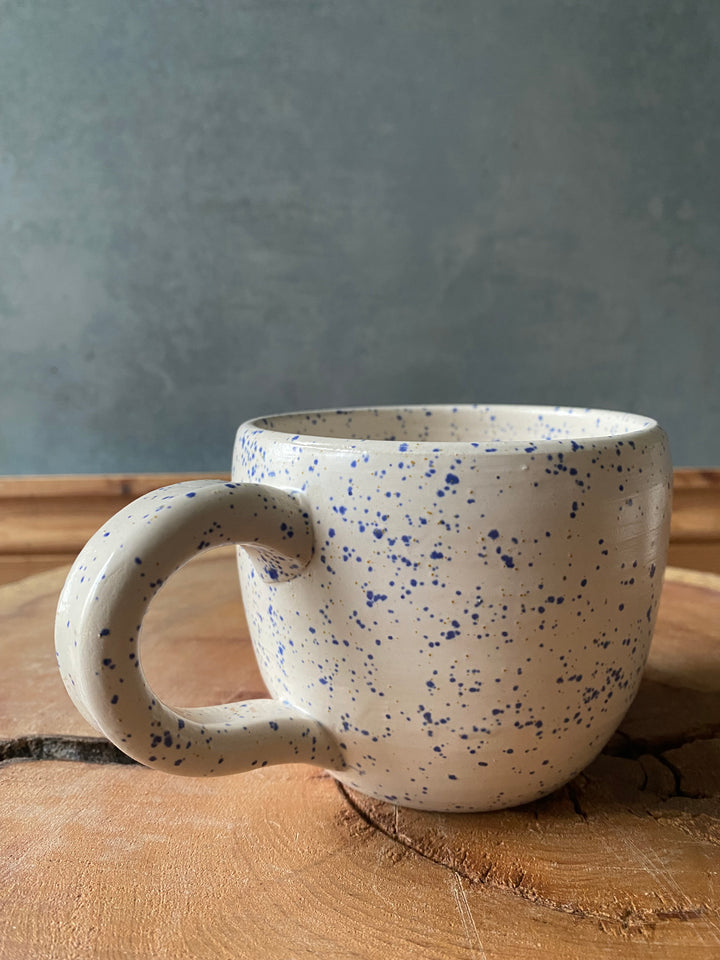 Speckled ceramic mug on a wooden surface with a grey background