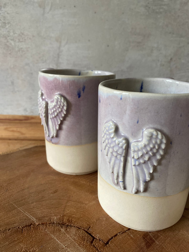 Two ceramic cups with hand-shaped embossments on a wooden surface.