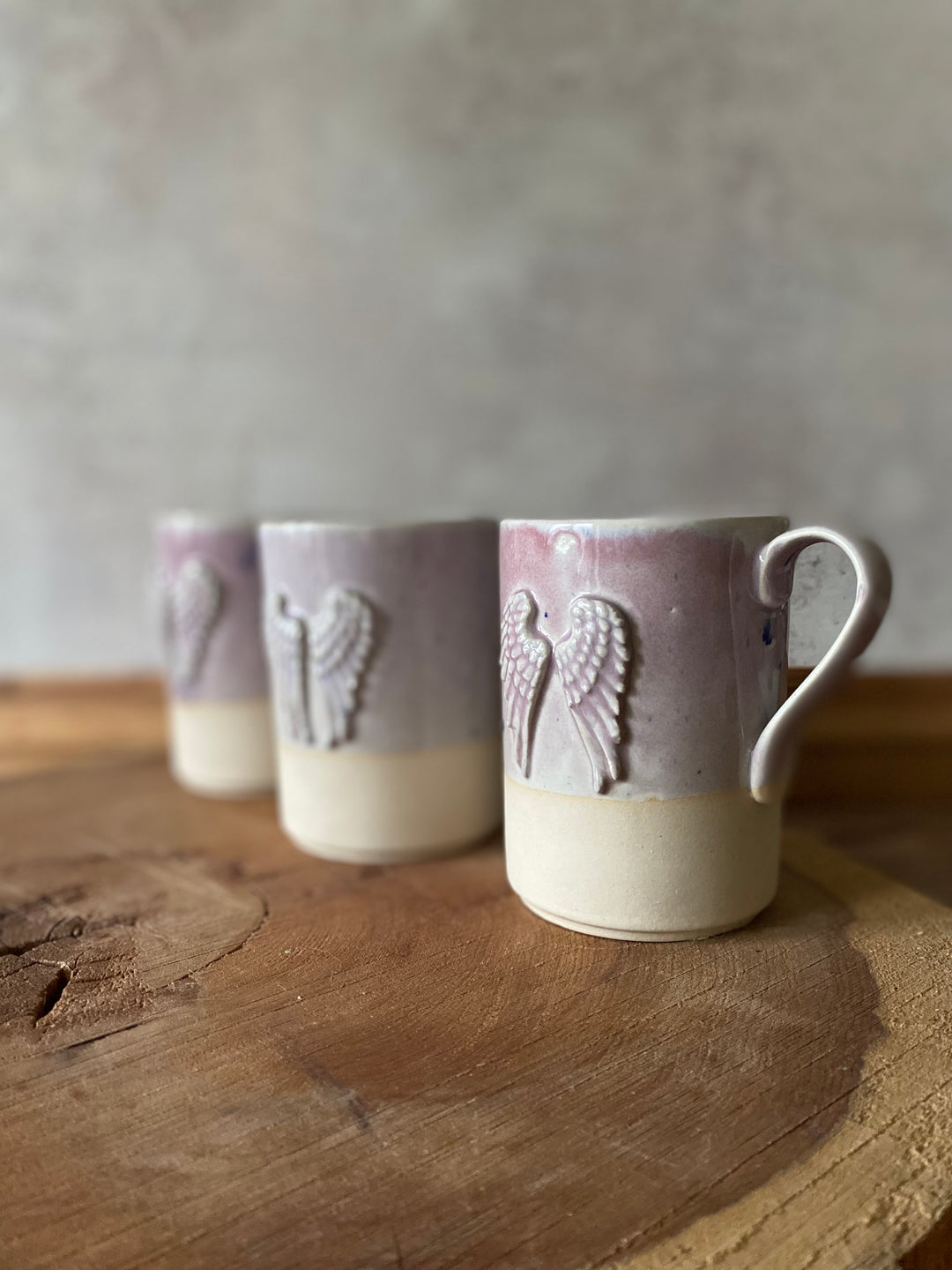 Three ceramic mugs with angel wings on a wooden surface and gray background