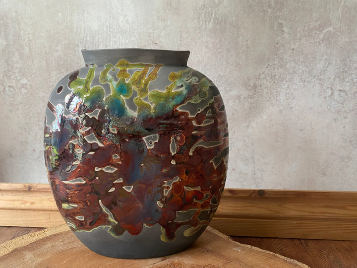Decorative ceramic vase with multicolored glaze on a wooden surface.