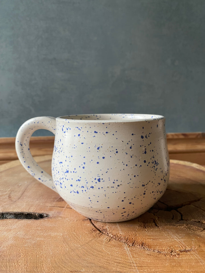 Speckled ceramic cup leaning against a wooden surface with a grey background