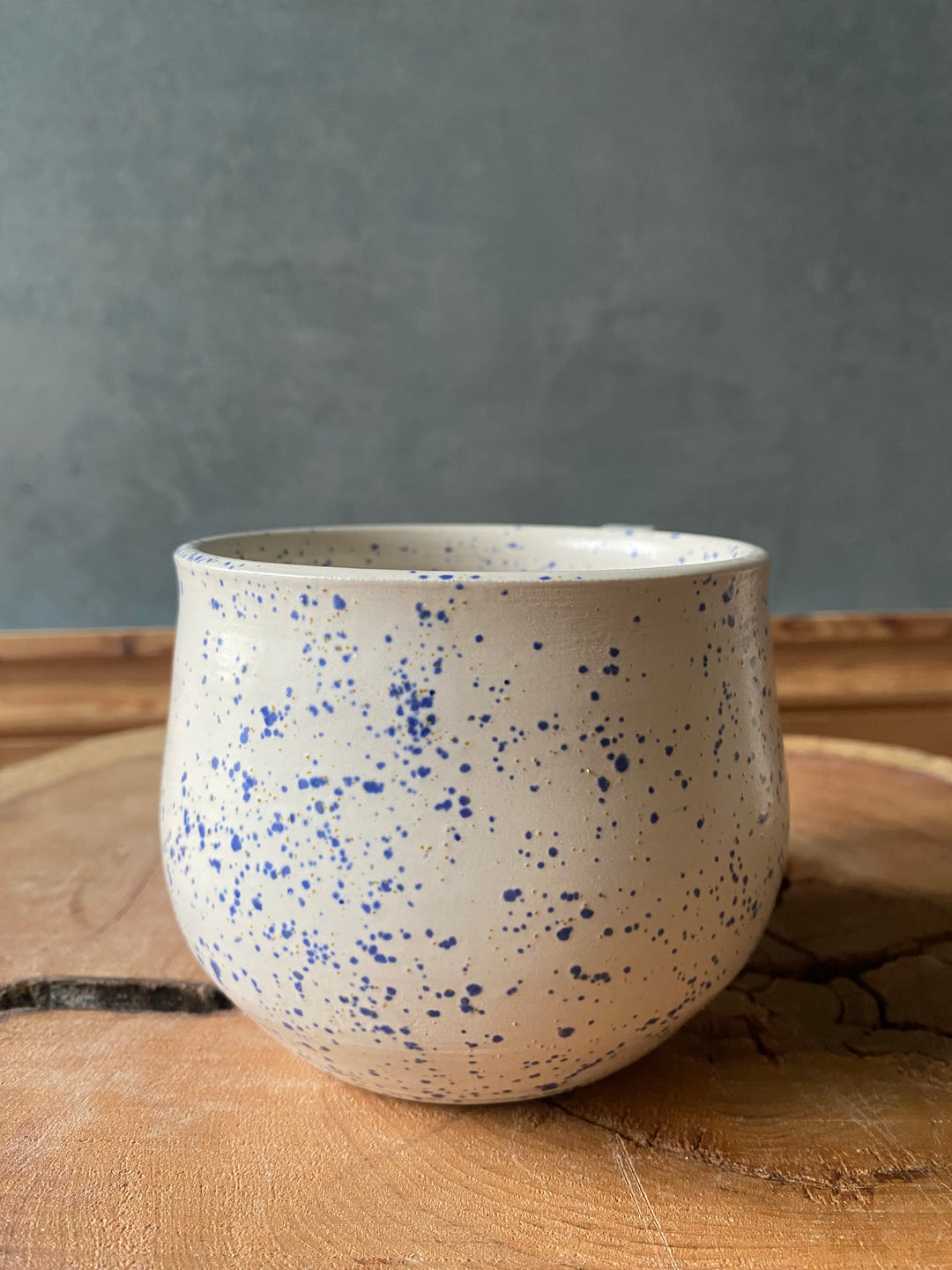Speckled ceramic cup on a wooden surface with a grey background