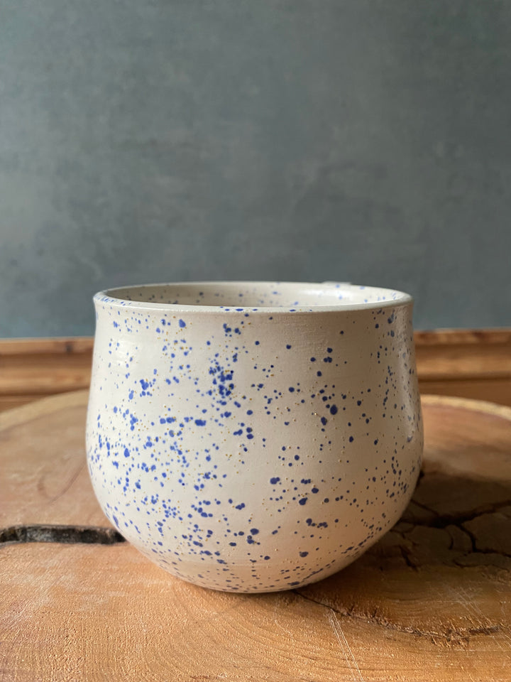 Speckled ceramic cup on a wooden surface with a grey background